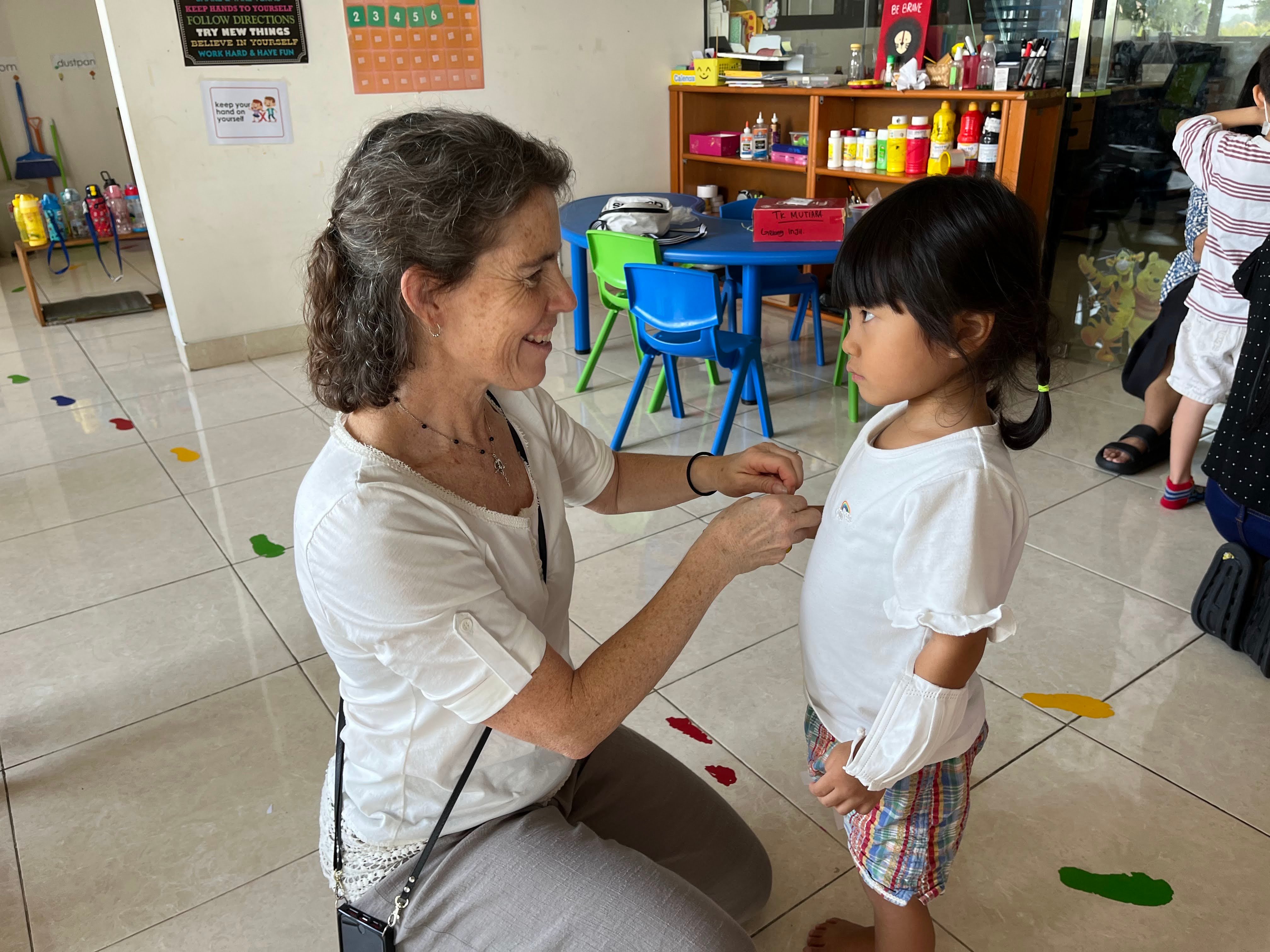 teacher putting on gospel message bracelet to little indonesian girl