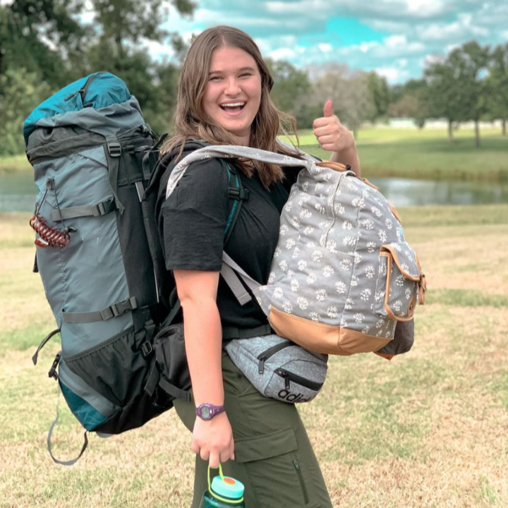 girl with backpack smiling in field